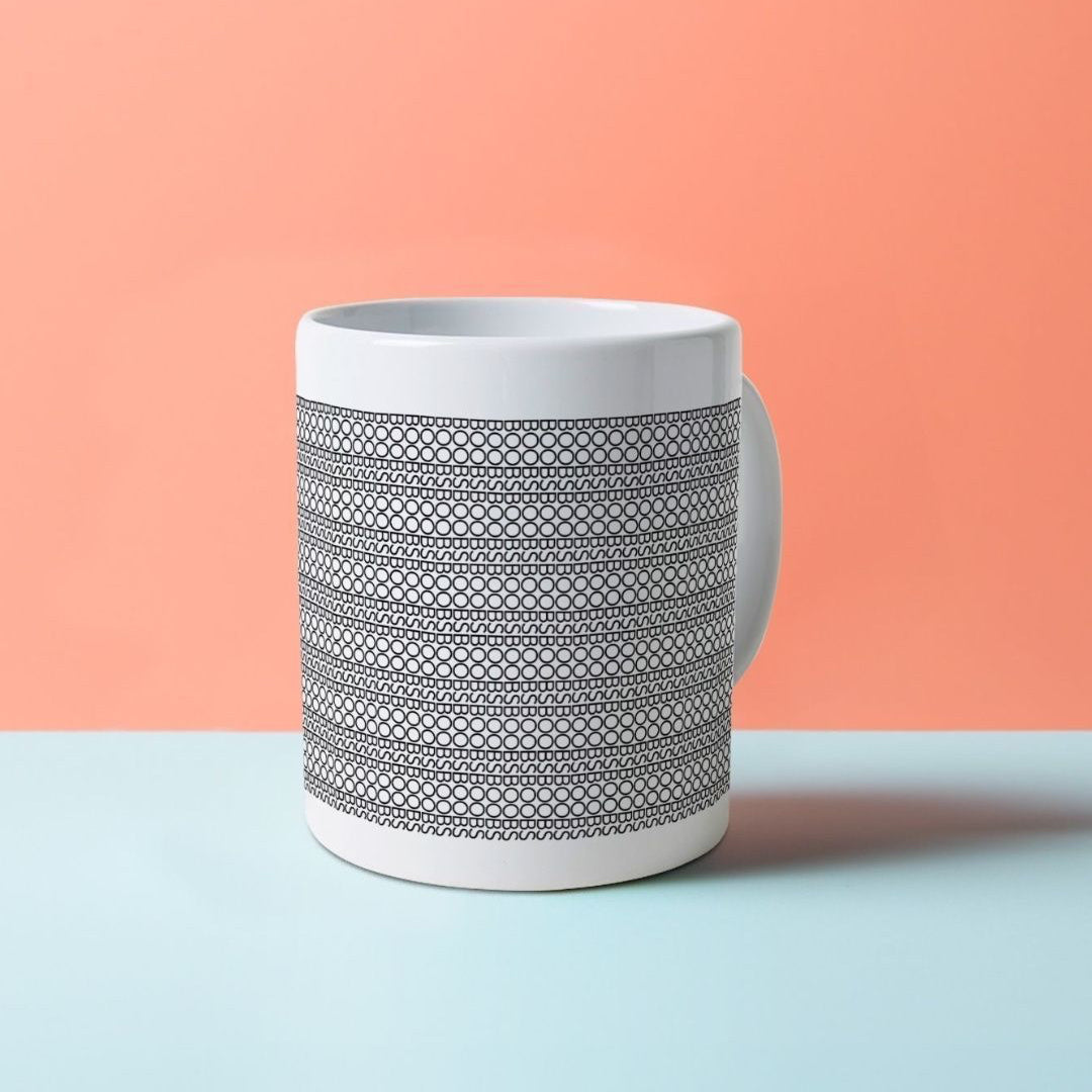 A white mug with black patterns on it, composed of the word BOOBS. Front view.