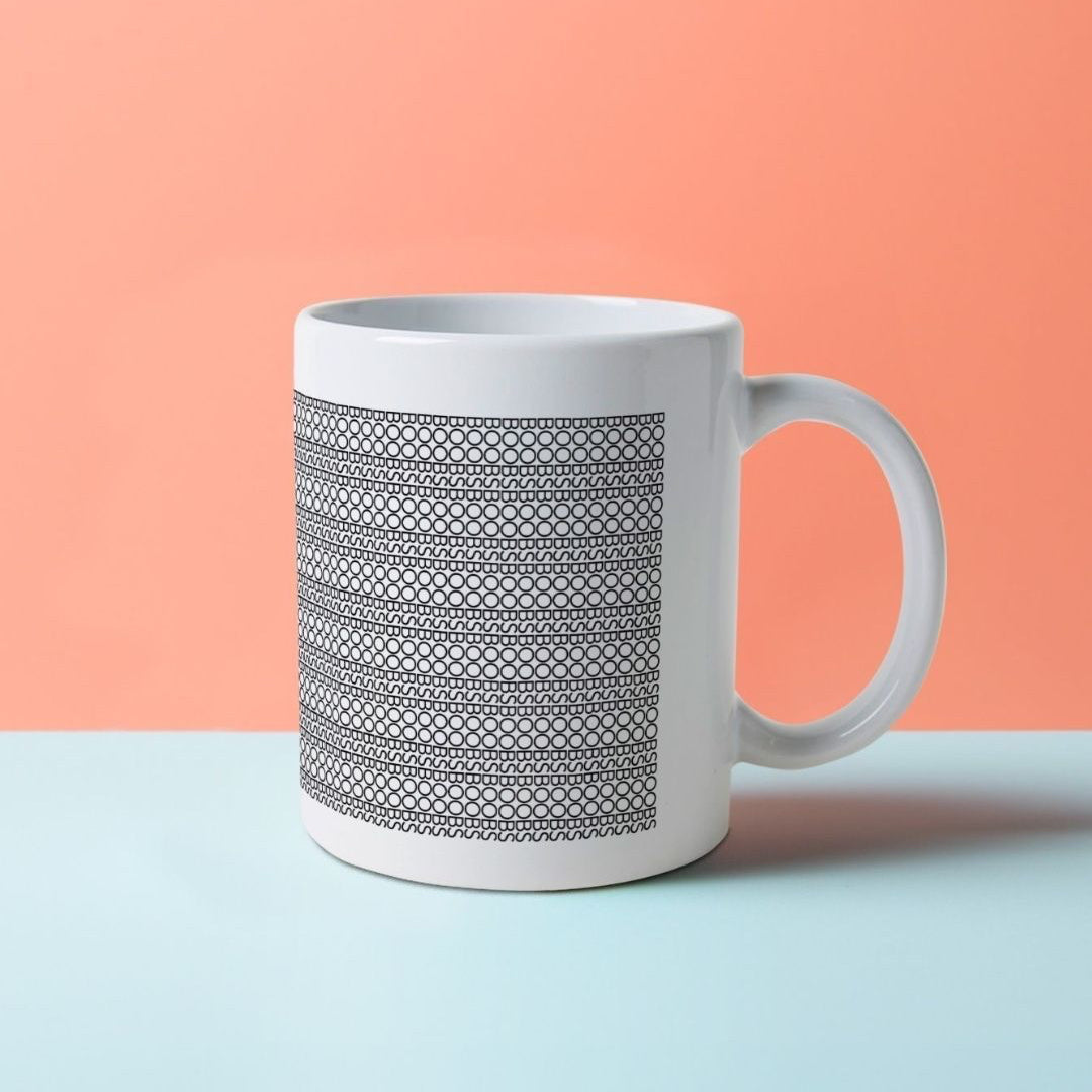 A white mug with black patterns on it, composed of the word BOOBS.
