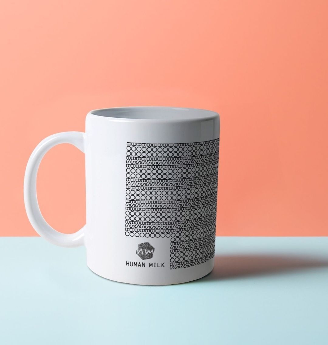 A white mug with black patterns on it, composed of the word BOOBS. Also, Human Milk logo.