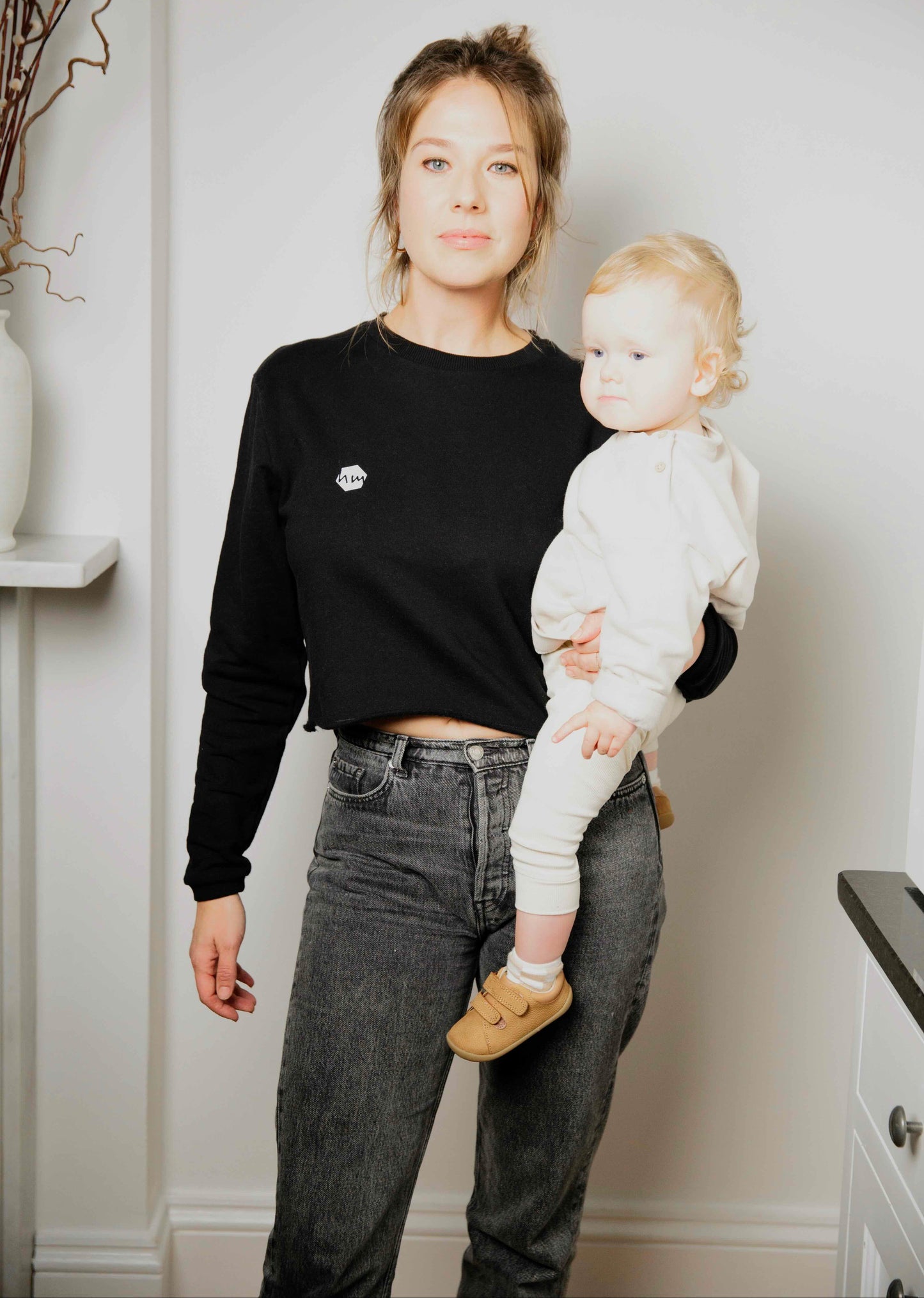 Woman wearing a human milk cropped sweater holding her baby in a home setting