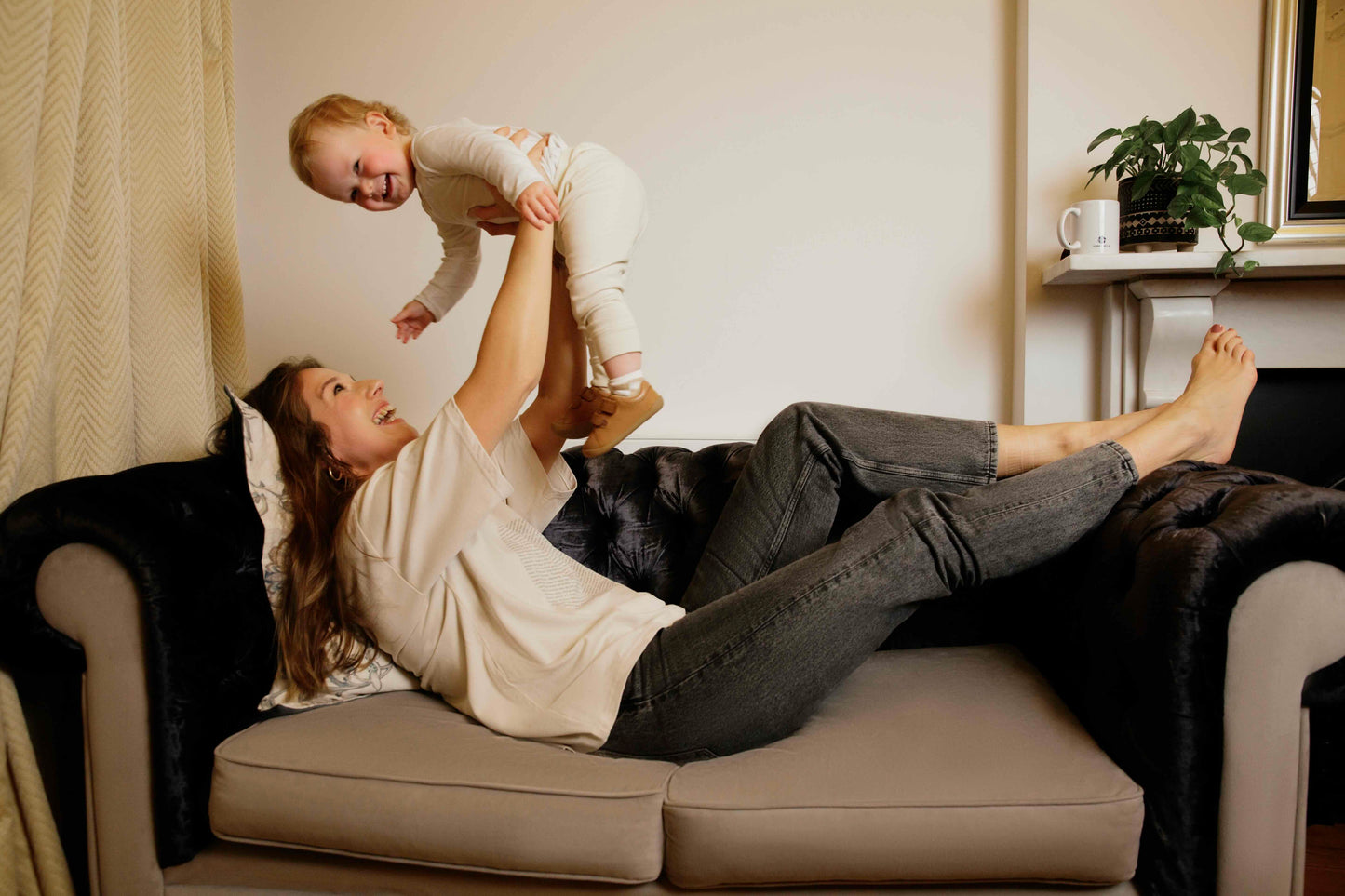 Woman wearing a human milk t-shirt lying on a couch holding a child in a living room setting