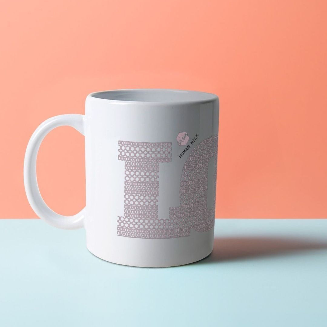A white ceramic mug with the word LOVE on it, composed of a pattern made with the word BOOB, with a Human Milk logo on it.