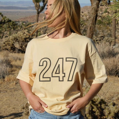 Woman wearing a yellow Human Milk t-shirt with '247' printed on it, in a desert setting