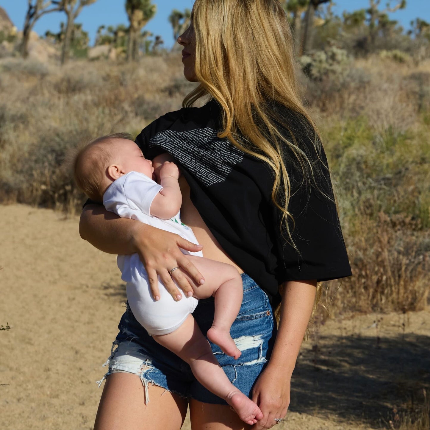Woman breastfeeding a baby in a desert landscape wearing a Human Milk Moon T-shirt
