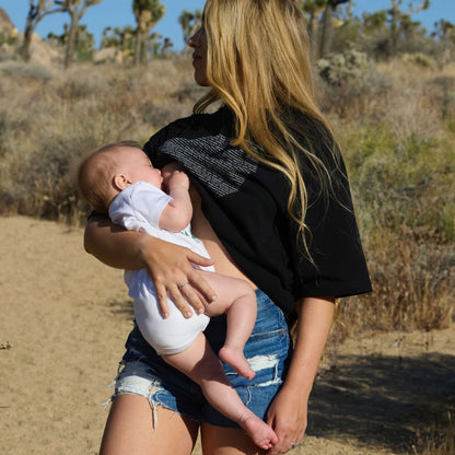 Woman breastfeeding a baby in a desert landscape wearing a Human Milk Moon T-shirt