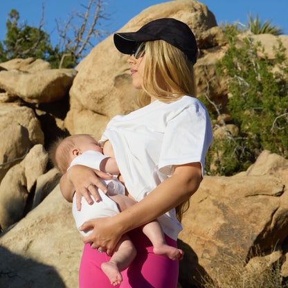 Woman BREASTFEEDING a baby outdoors in a rocky landscape, wearing a Human Milk 'RESILIENT' T-shirt