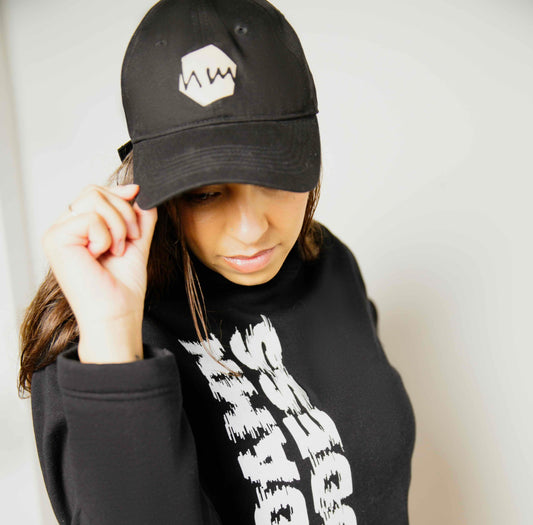 Woman wearing a black hoodie with white text and a matching black cap with a human milk logo.