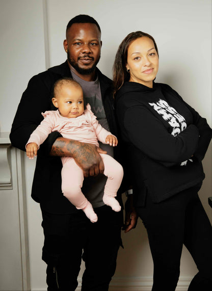 Mother, father and baby posing together, wearing Human Milk clothes in a room with a white background