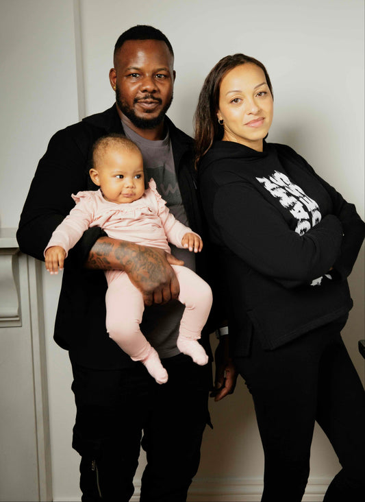 Mother, father and baby posing together, wearing Human Milk clothes in a room with a white background