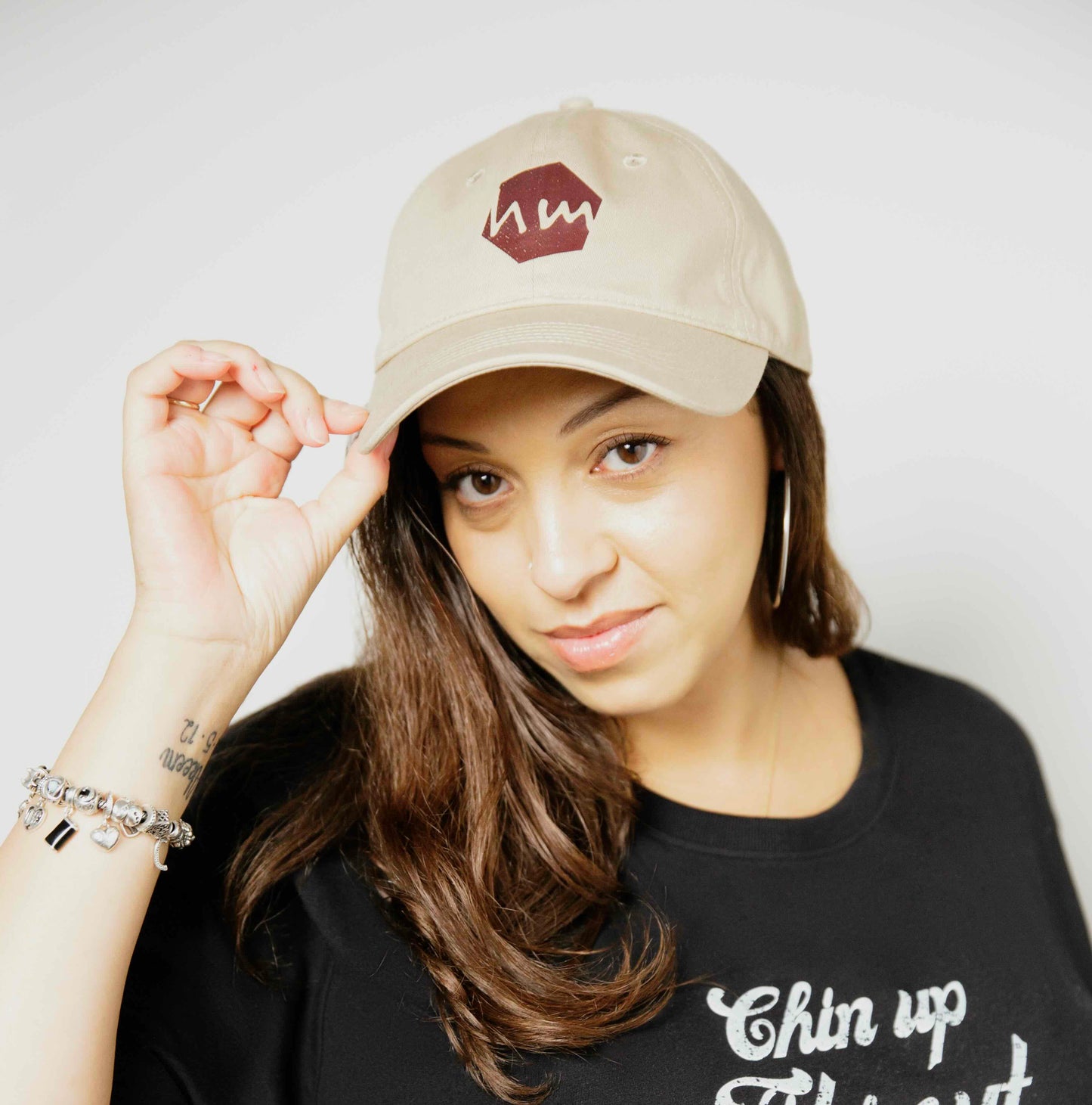 Woman wearing a black t-shirt with text and a beige human milk logo cap on a plain background
