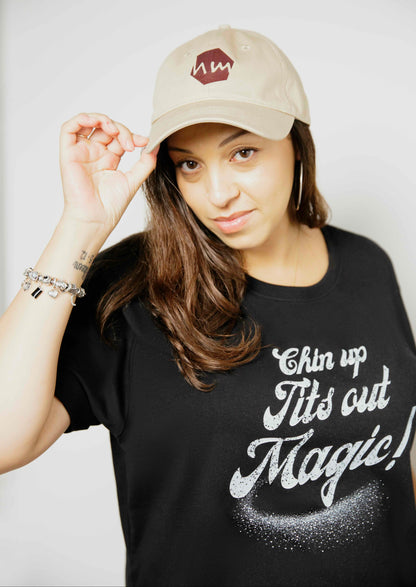Woman wearing a black human milk t-shirt with text and a beige human milk logo cap on a plain background