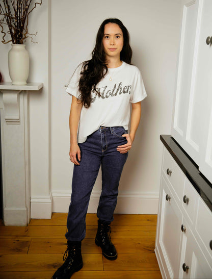 Woman wearing a white human milk t-shirt with text and blue jeans standing in a room with white walls and wooden floor.