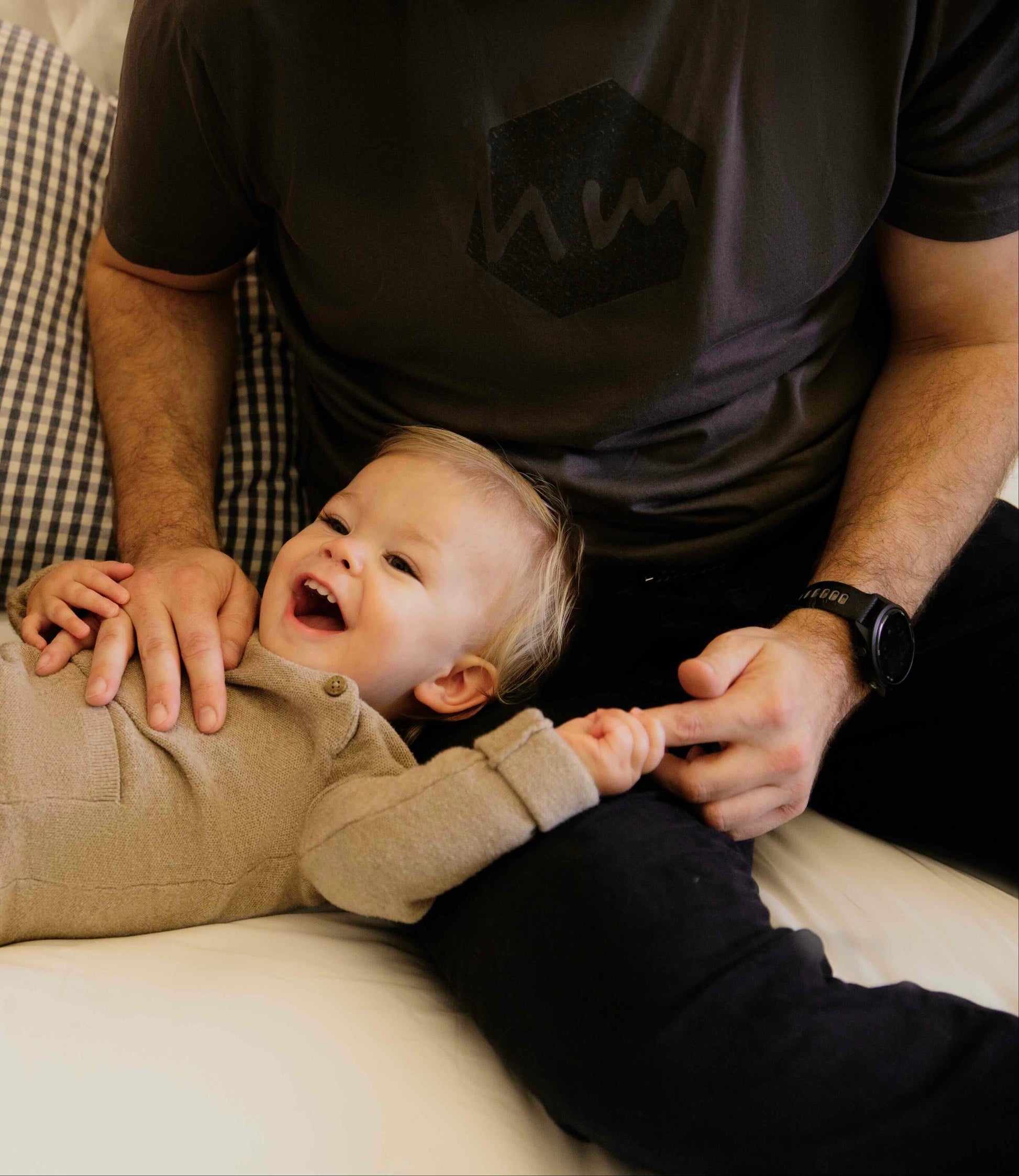 Baby lying on a couch laughing with his ad who is wearing a human milk t-shirt