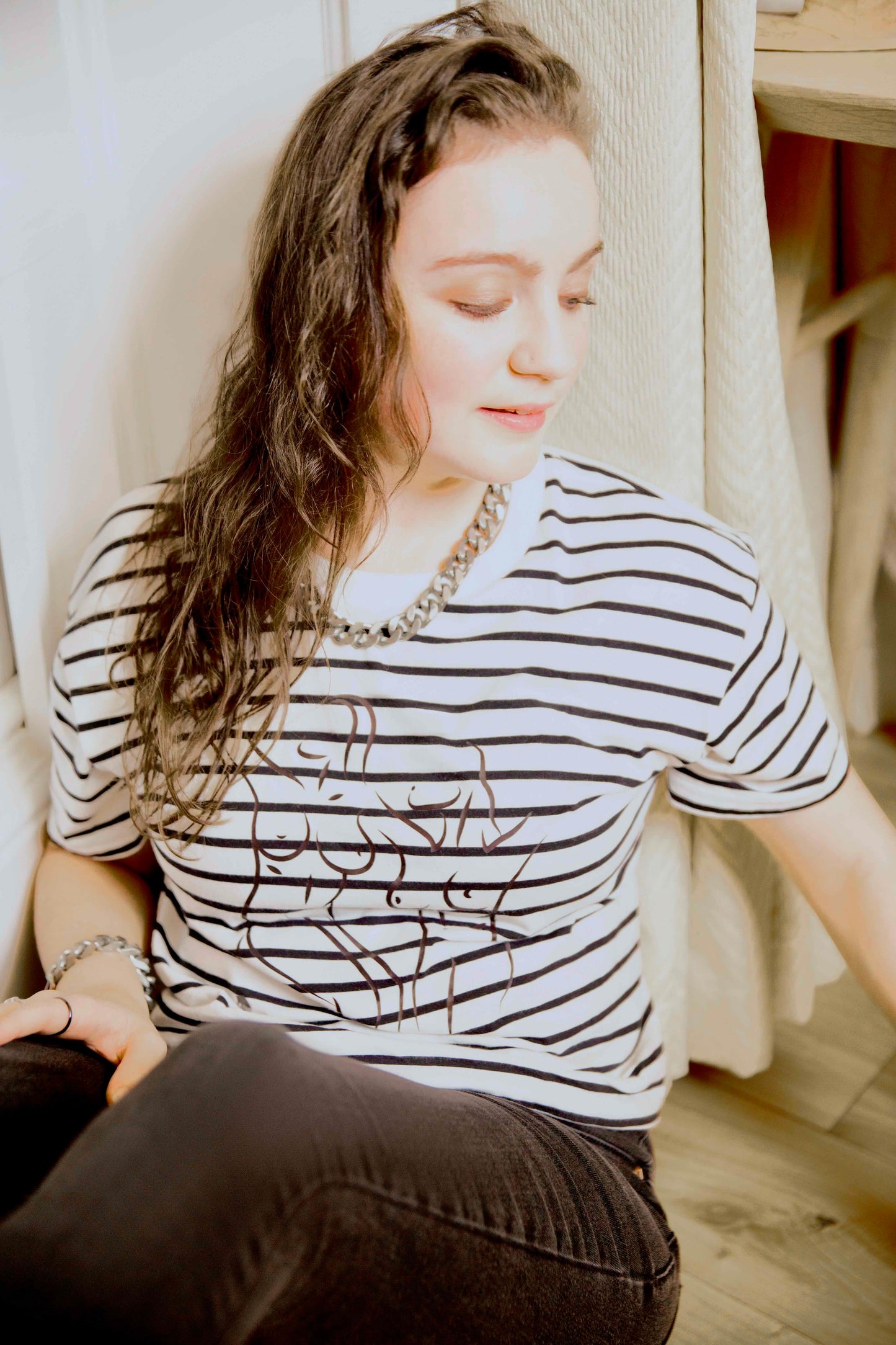 Woman wearing a black and white striped human milk t-shirt sitting indoors.