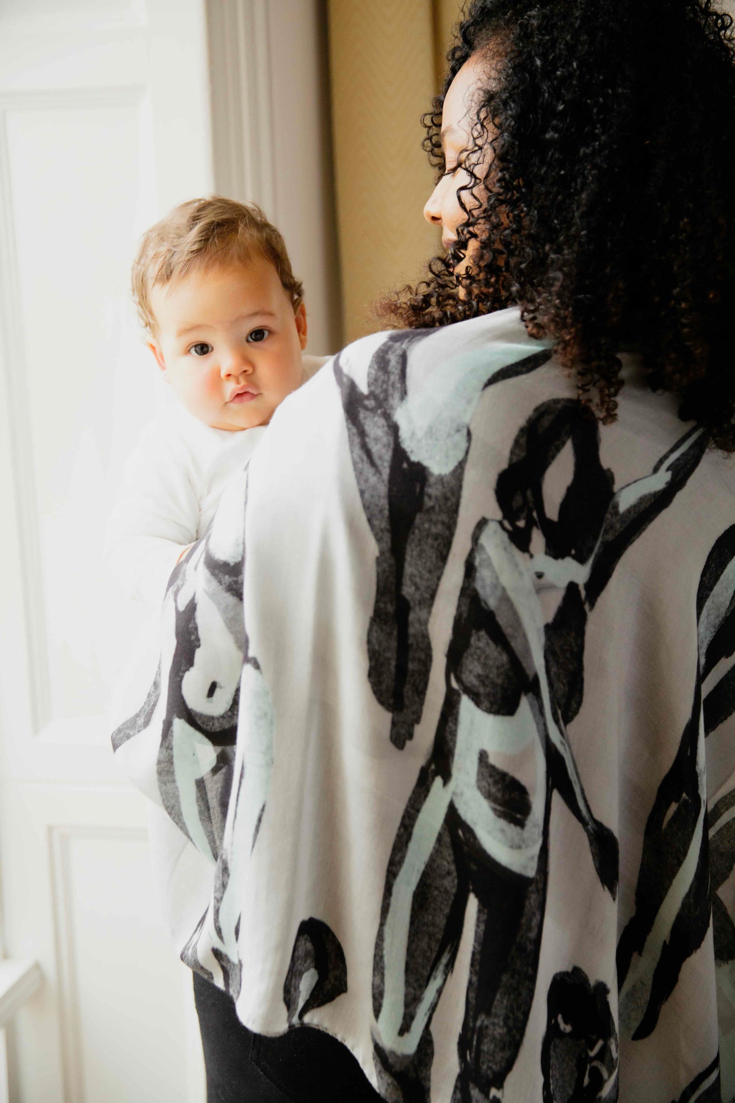 Woman wearing a grey, black and teal human milk scarf, holding her baby.