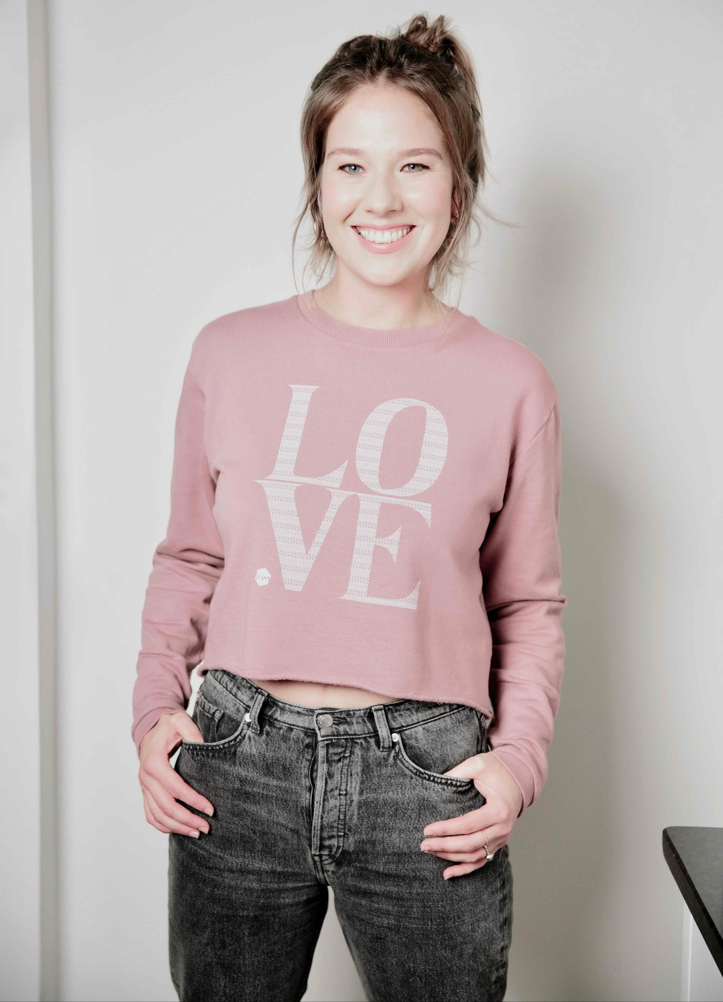 Woman wearing a pink 'LOVE' Human Milk sweatshirt and black jeans against a plain background
