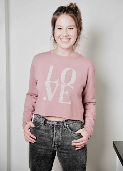 Woman wearing a pink 'LOVE' Human Milk sweatshirt and black jeans against a plain background