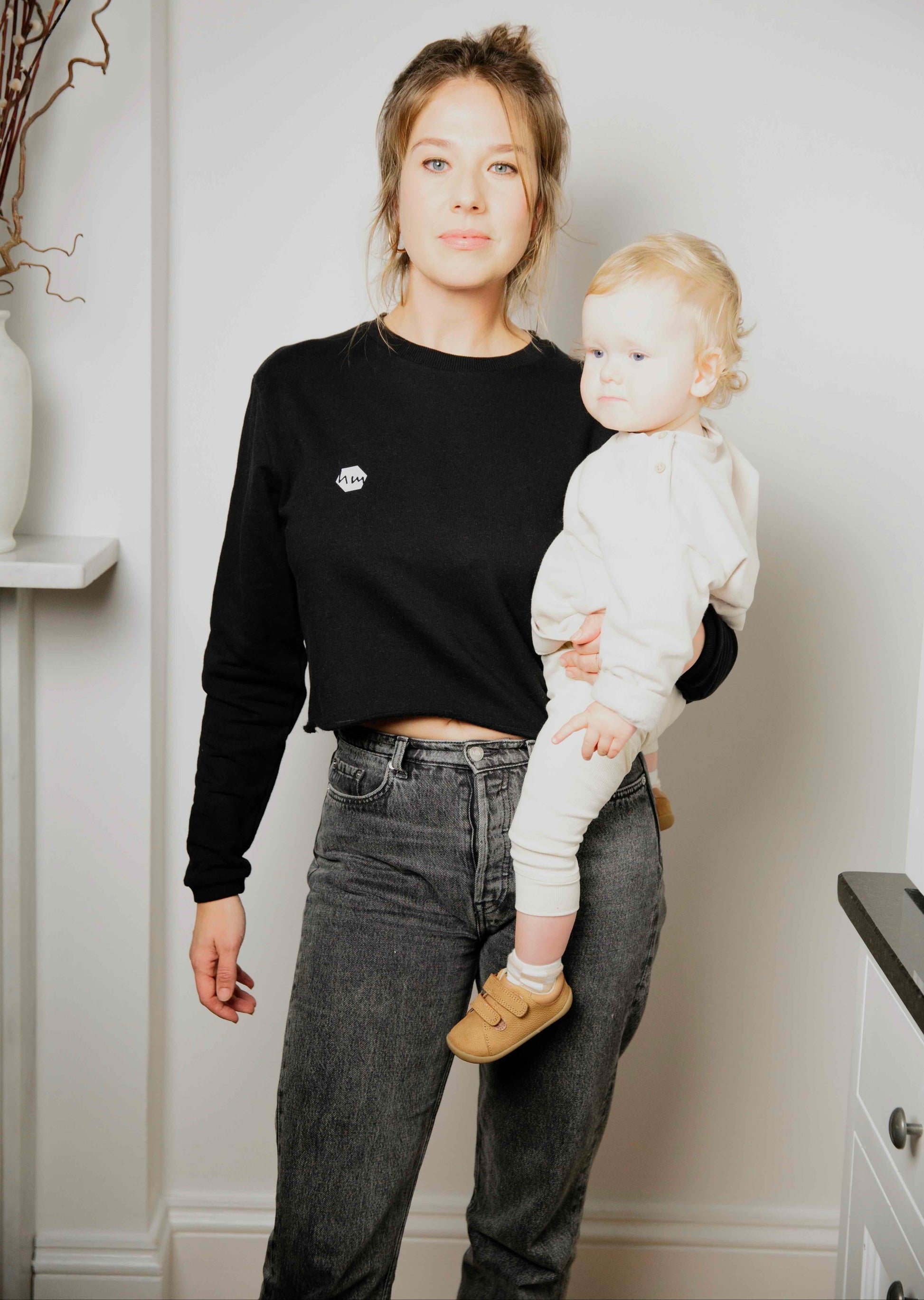 Woman  wearing a human milk cropped sweater holding her baby in a home setting