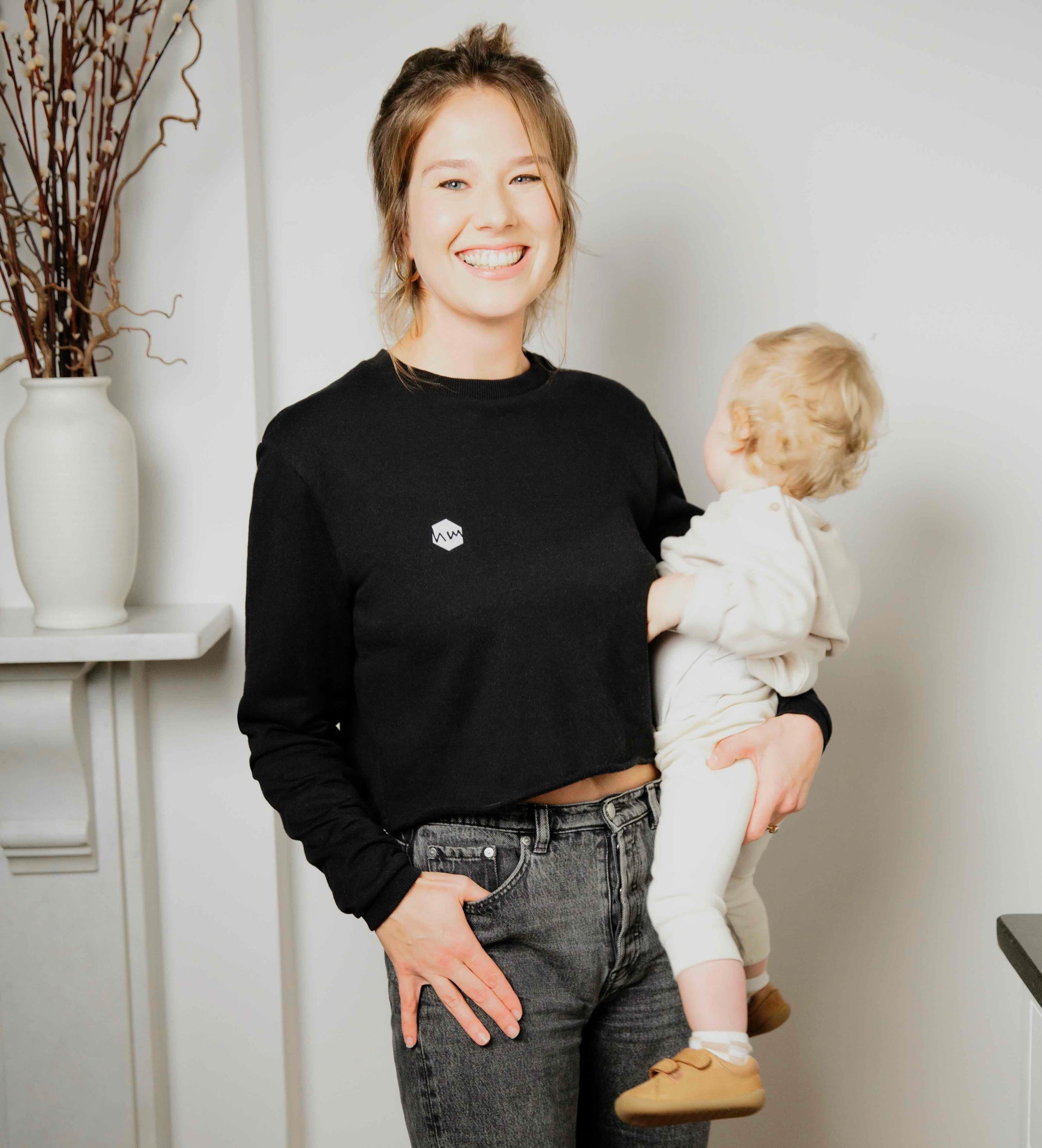 Woman wearing a human milk cropped sweater holding her child indoors with a neutral background