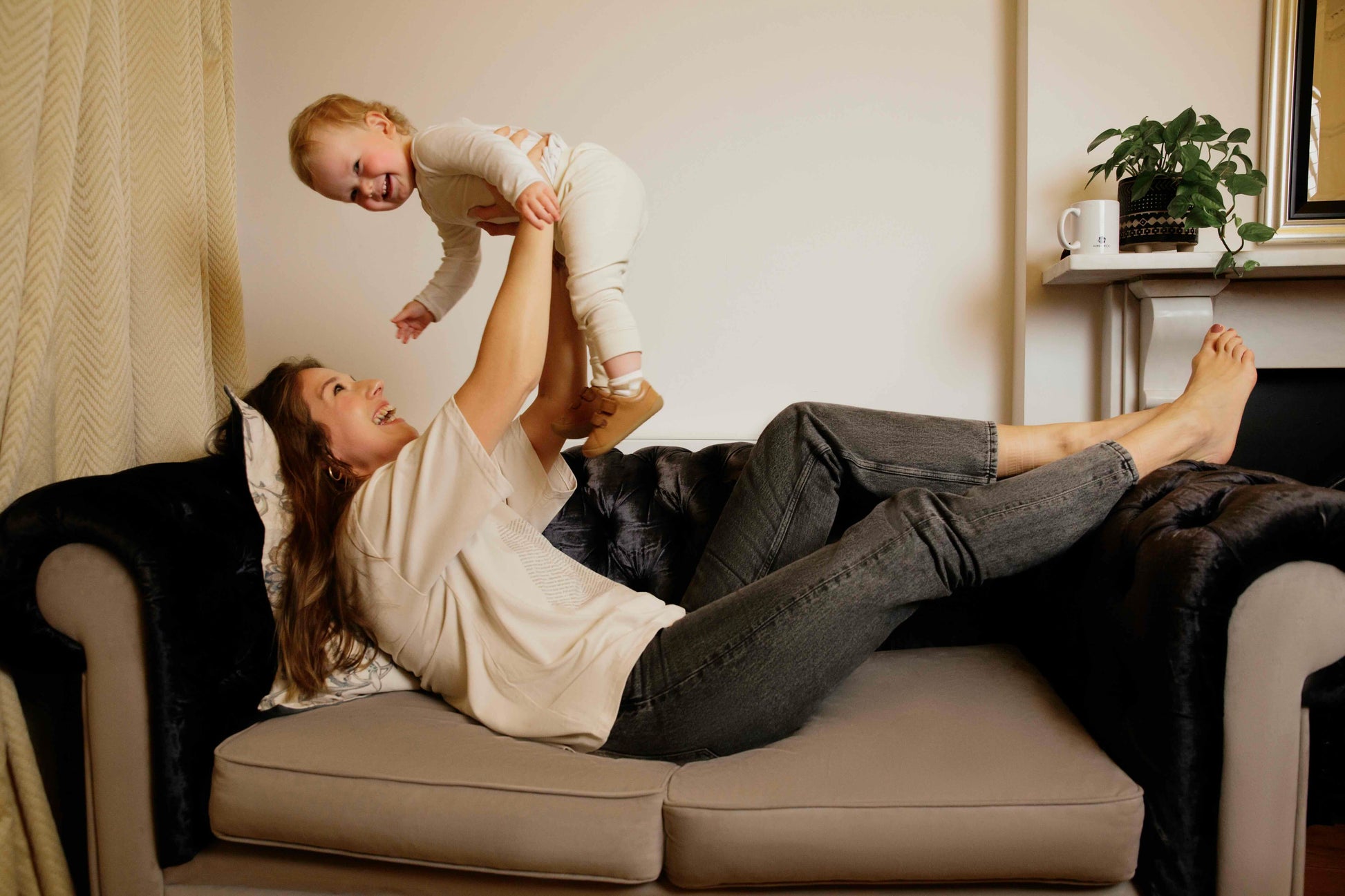 Woman wearing a human milk t-shirt lying on a couch holding a child in a living room setting