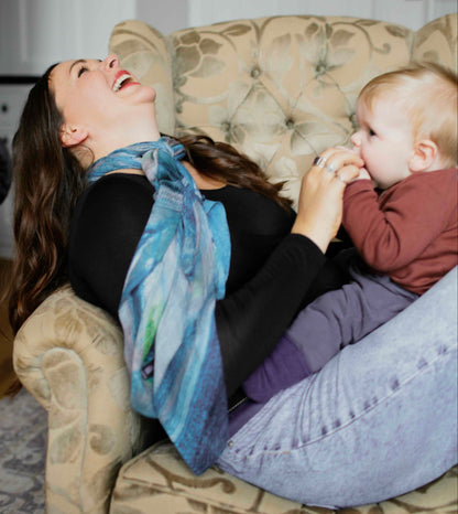 Woman lying on a couch wearing a human milk scarf with a baby, both laughing