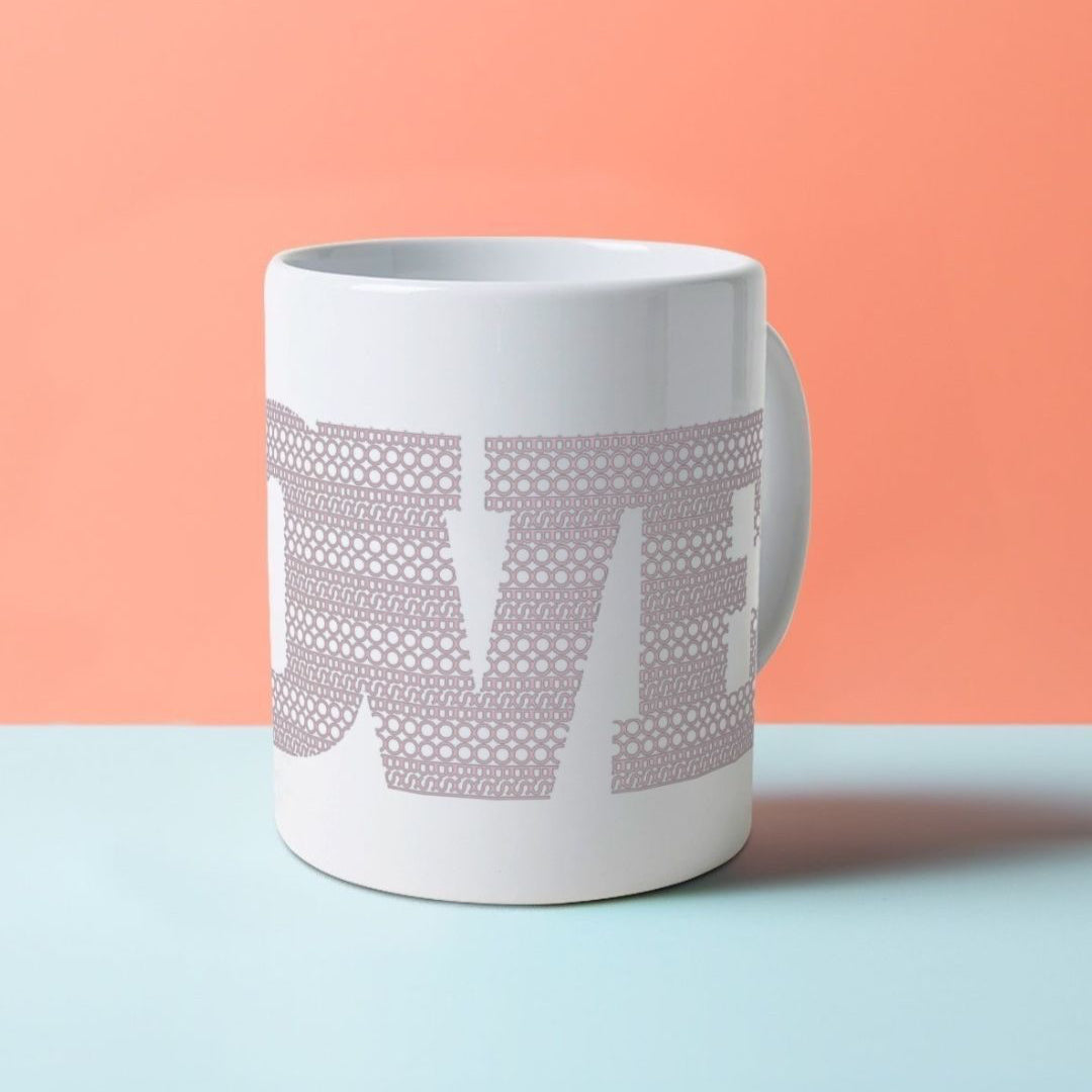 A white ceramic mug with the word LOVE on it, composed of a pattern made with the word BOOB.