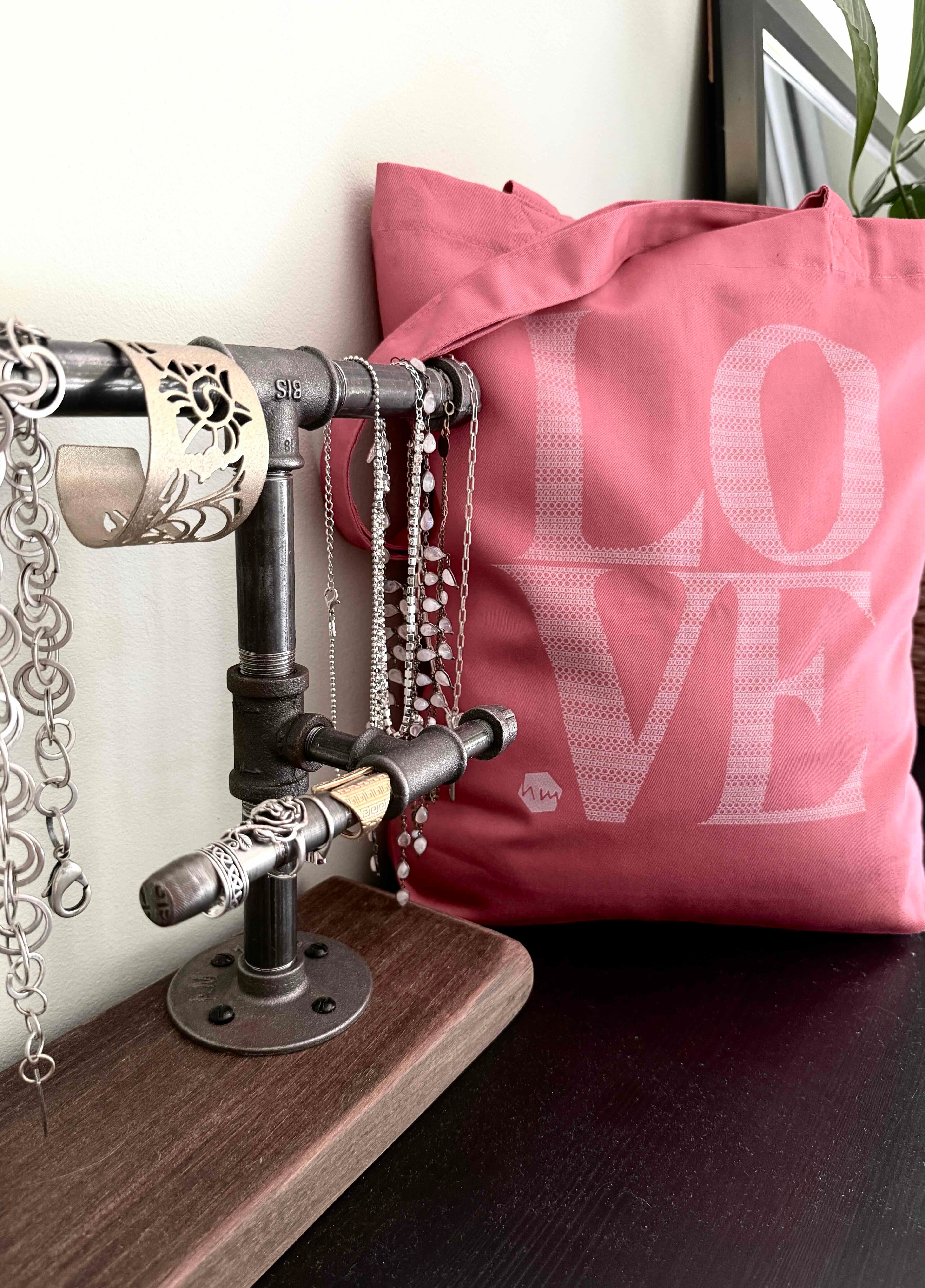 Pink pillow with 'LOVE' text next to a metal pipe jewelry holder on a wooden surface.