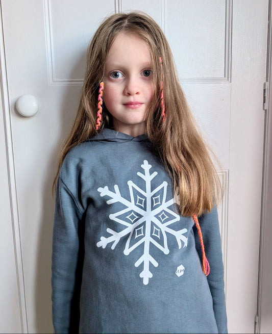 Young girl with long blonde hair wearing a human milk snowflake hoodie in blue