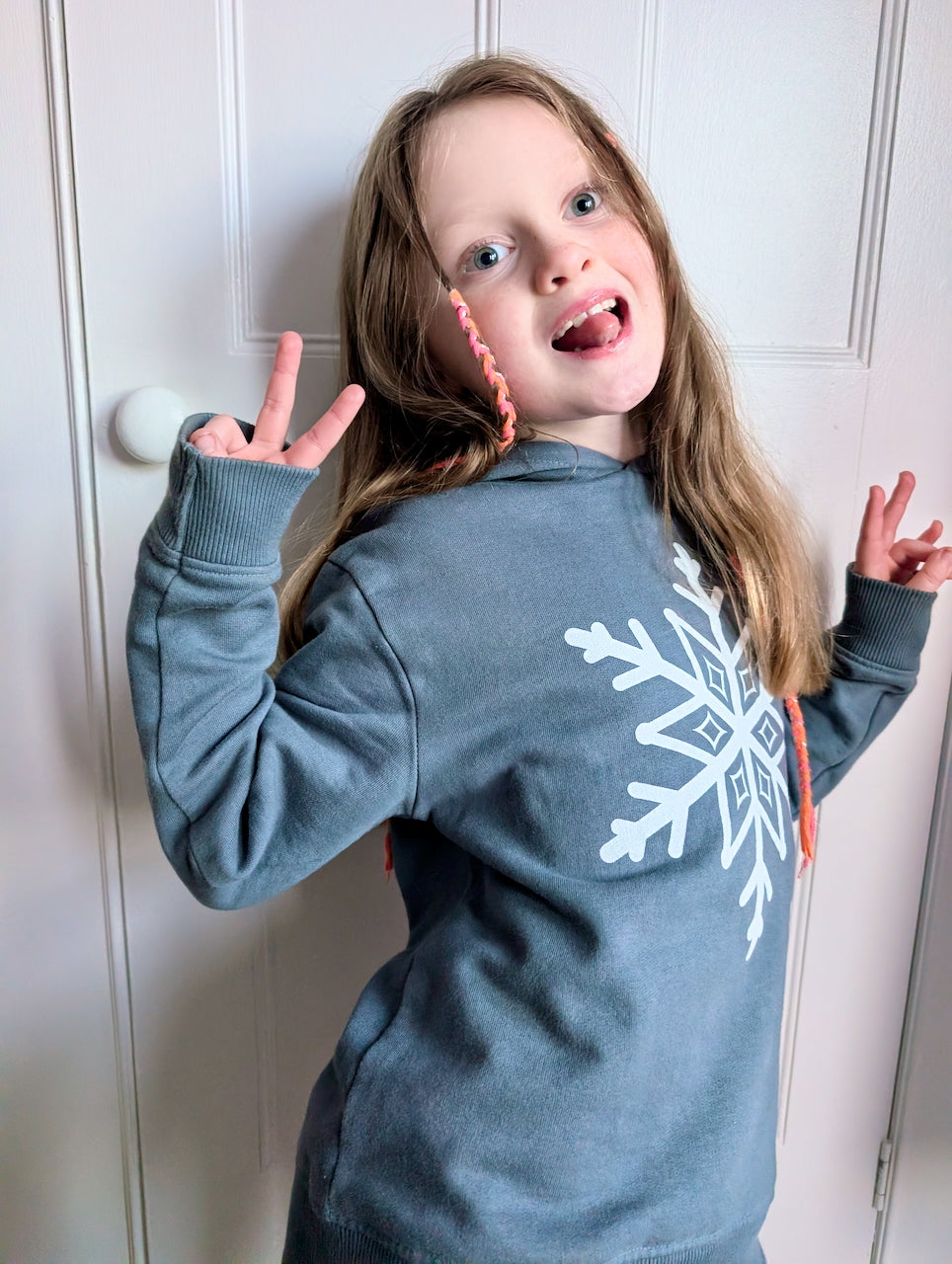 Young girl with long blonde hair wearing a human milk snowflake hoodie in blue