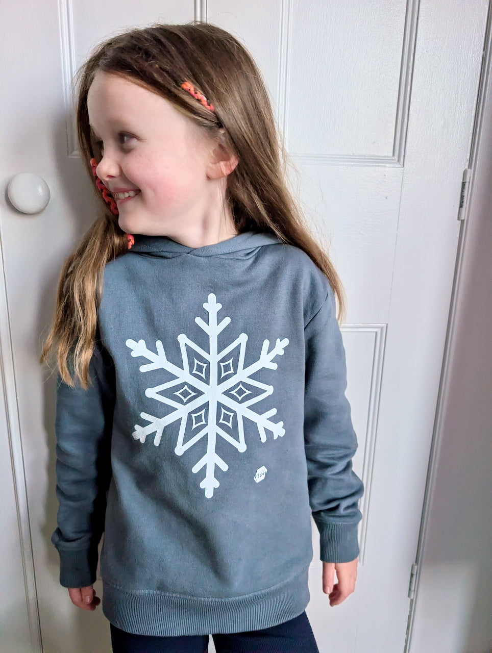 Young girl with long blonde hair wearing a human milk snowflake hoodie in blue