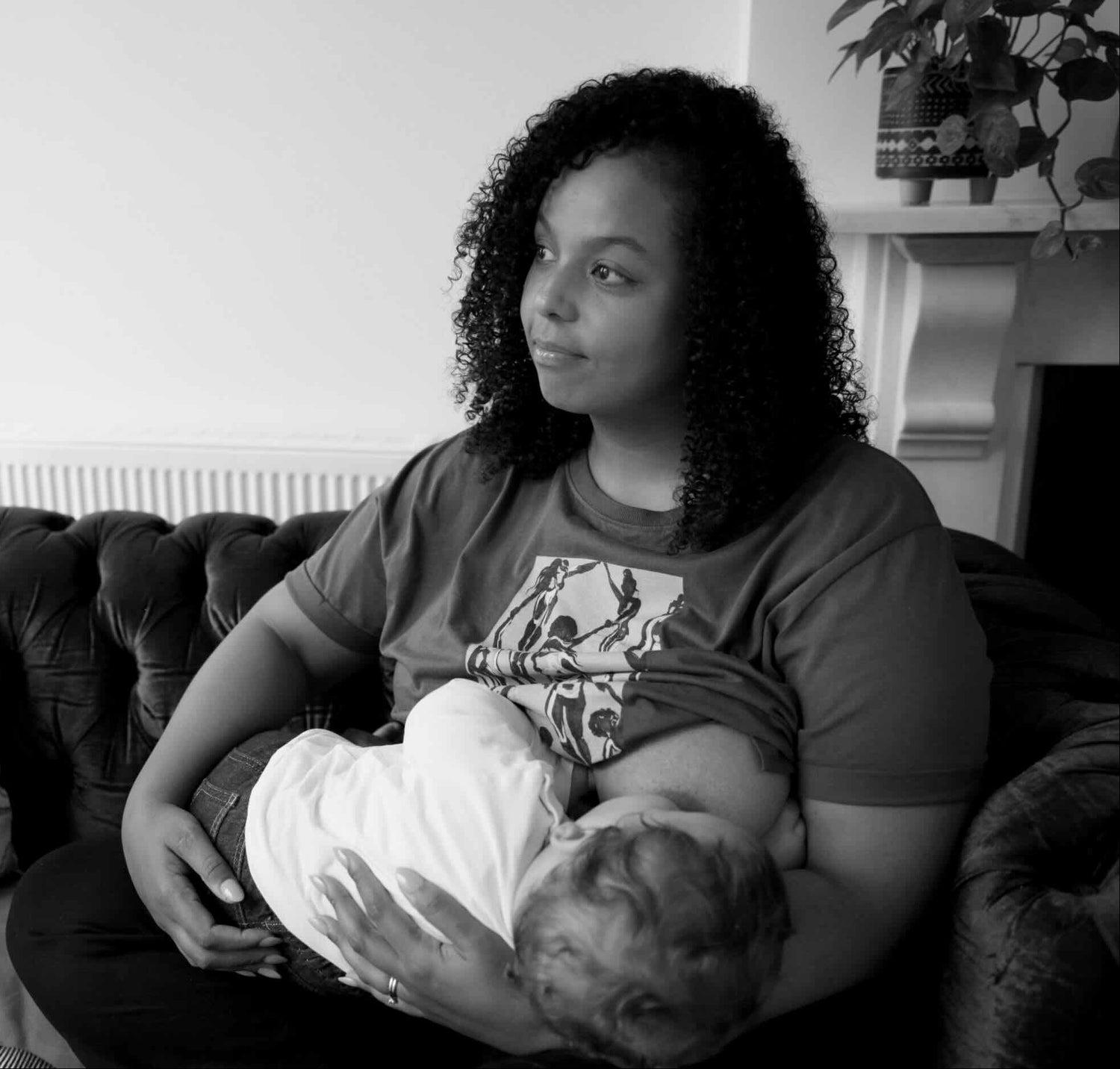 Woman breastfeeding her baby on a couch in a home setting, wearing a human milk t-shirt