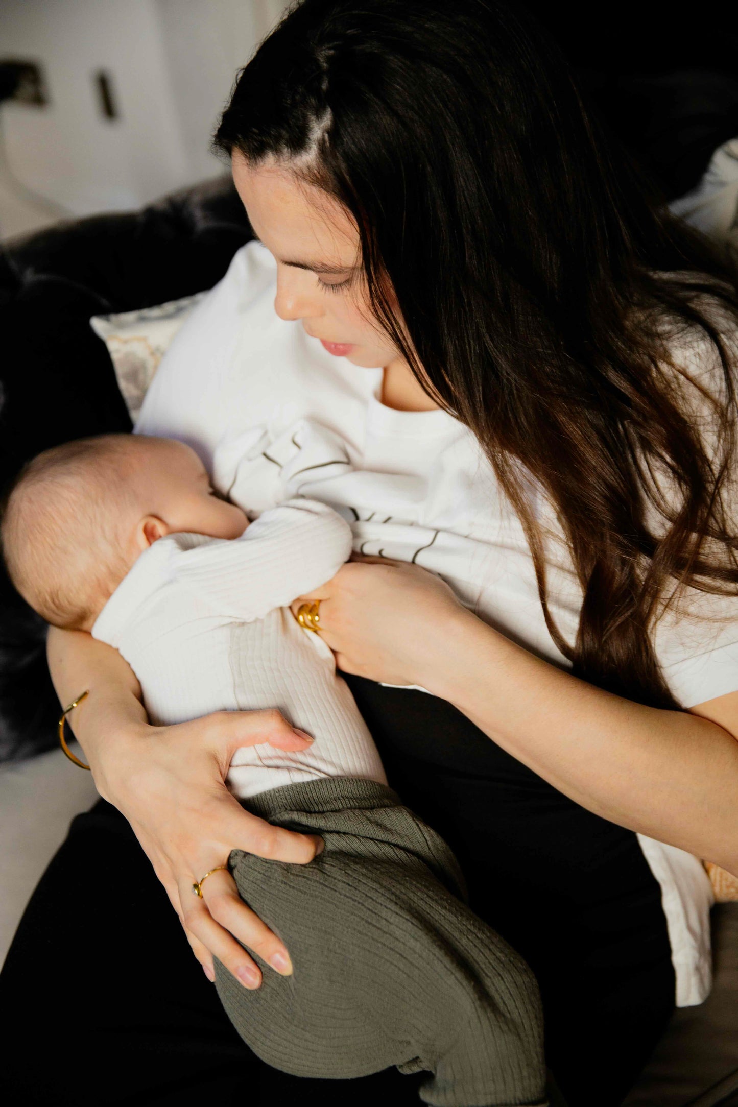 Woman wearing a human milk t-shirt holding a baby wrapped in a white blanket indoors.