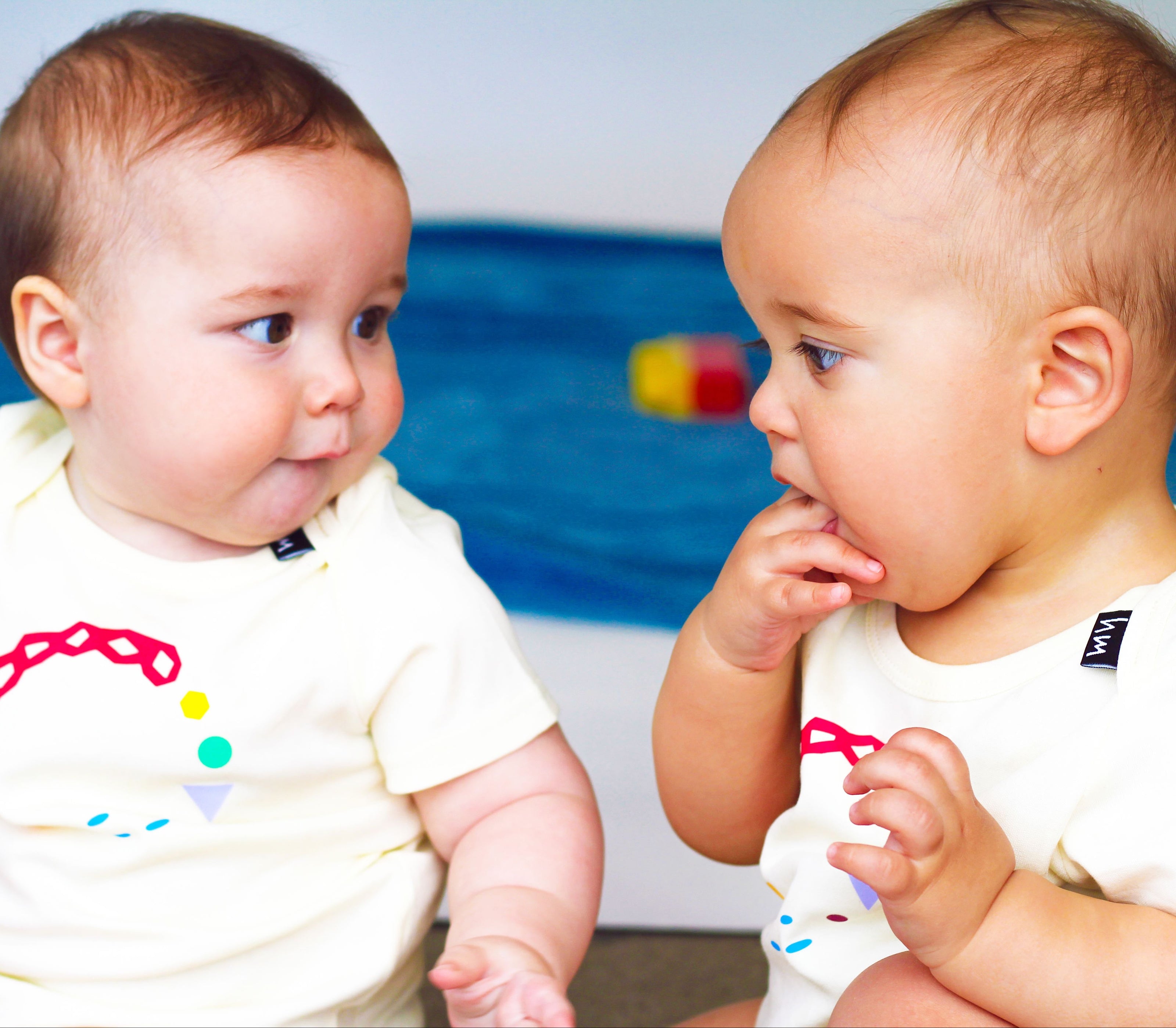 Two babies wearing Human Milk onesies with colorful designs sitting next to each other.